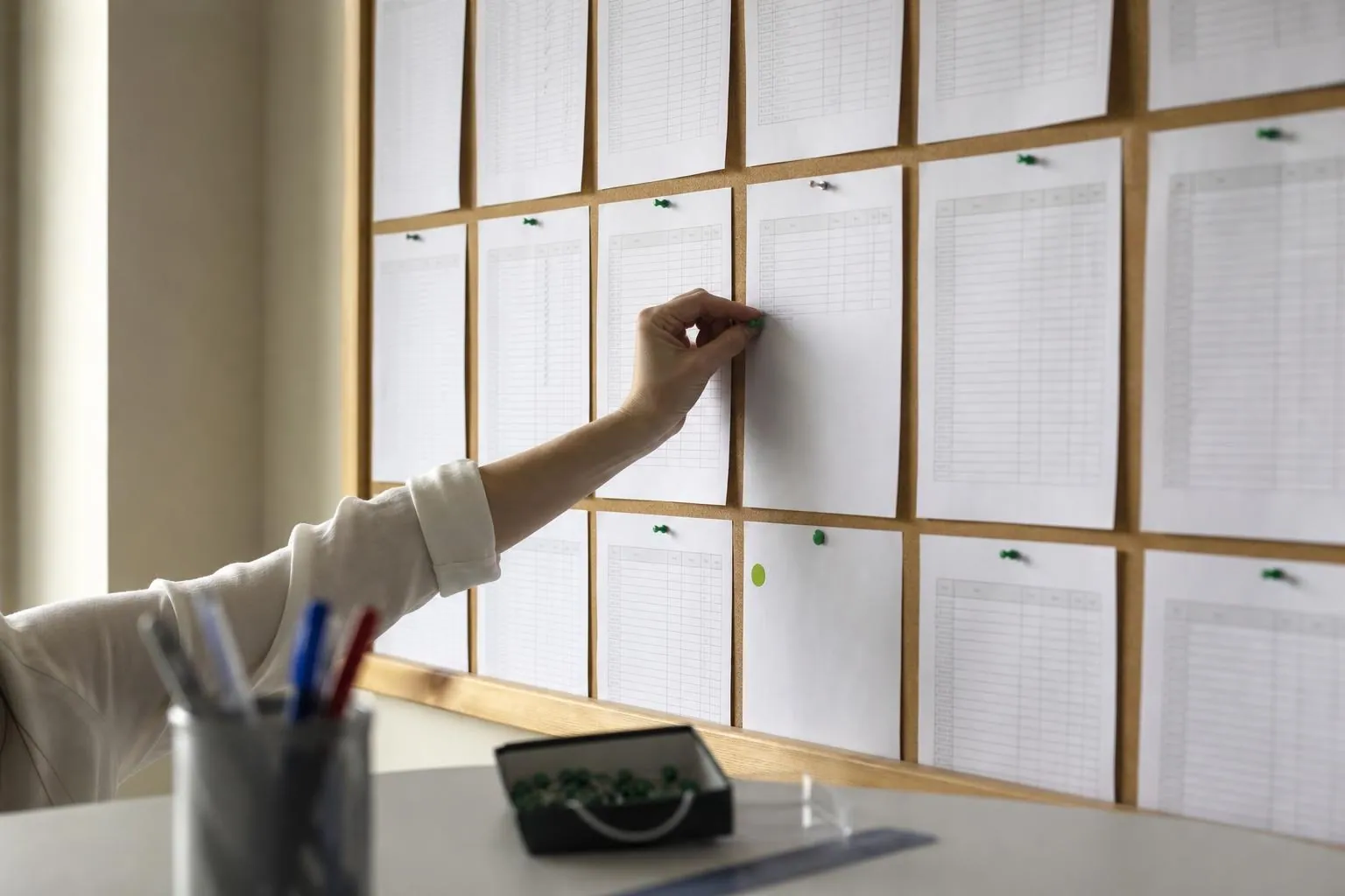 Une main epingle une liste imprimee et cochee au crayon sur un tableau en liege dans un bureau